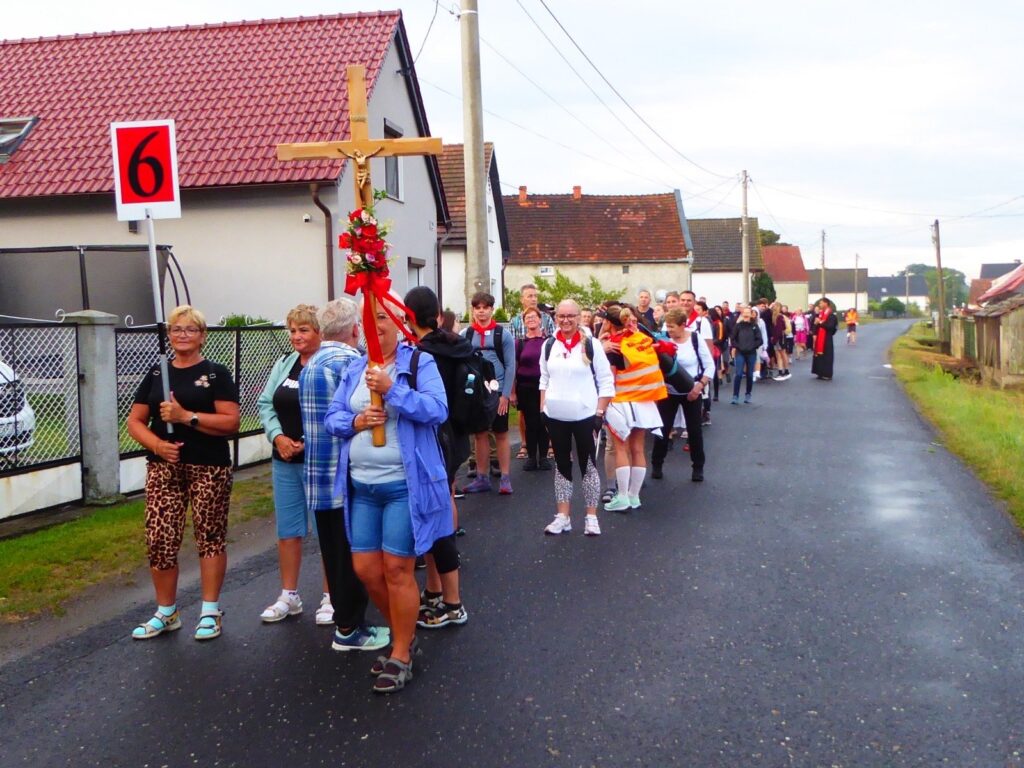 Krzyż pielgrzymkowy przystrojony czerwonymi wstążkami na czele grupy